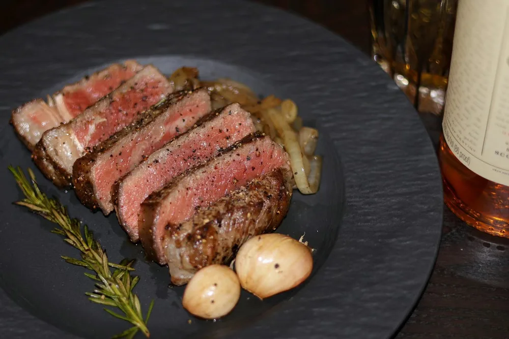 Close-up of medium-rare sliced steak on a slate plate with rosemary and roasted garlic
